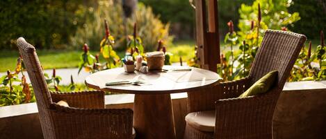 Une table ronde en bois, entourée de chaises en osier, installée dans un jardin verdoyant et fleuri.