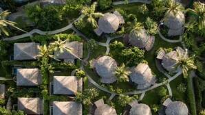 Vista aérea de un resort con cabañas de techo de paja dispuestas en grupos, rodeado de exuberante follaje y palmeras.