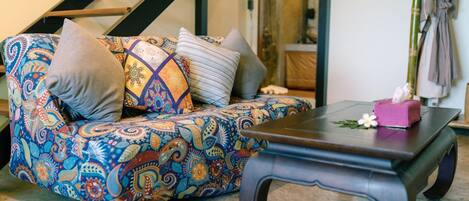 A patterned sofa with cushions, a dark wooden coffee table with a tissue box, and a staircase in the background.