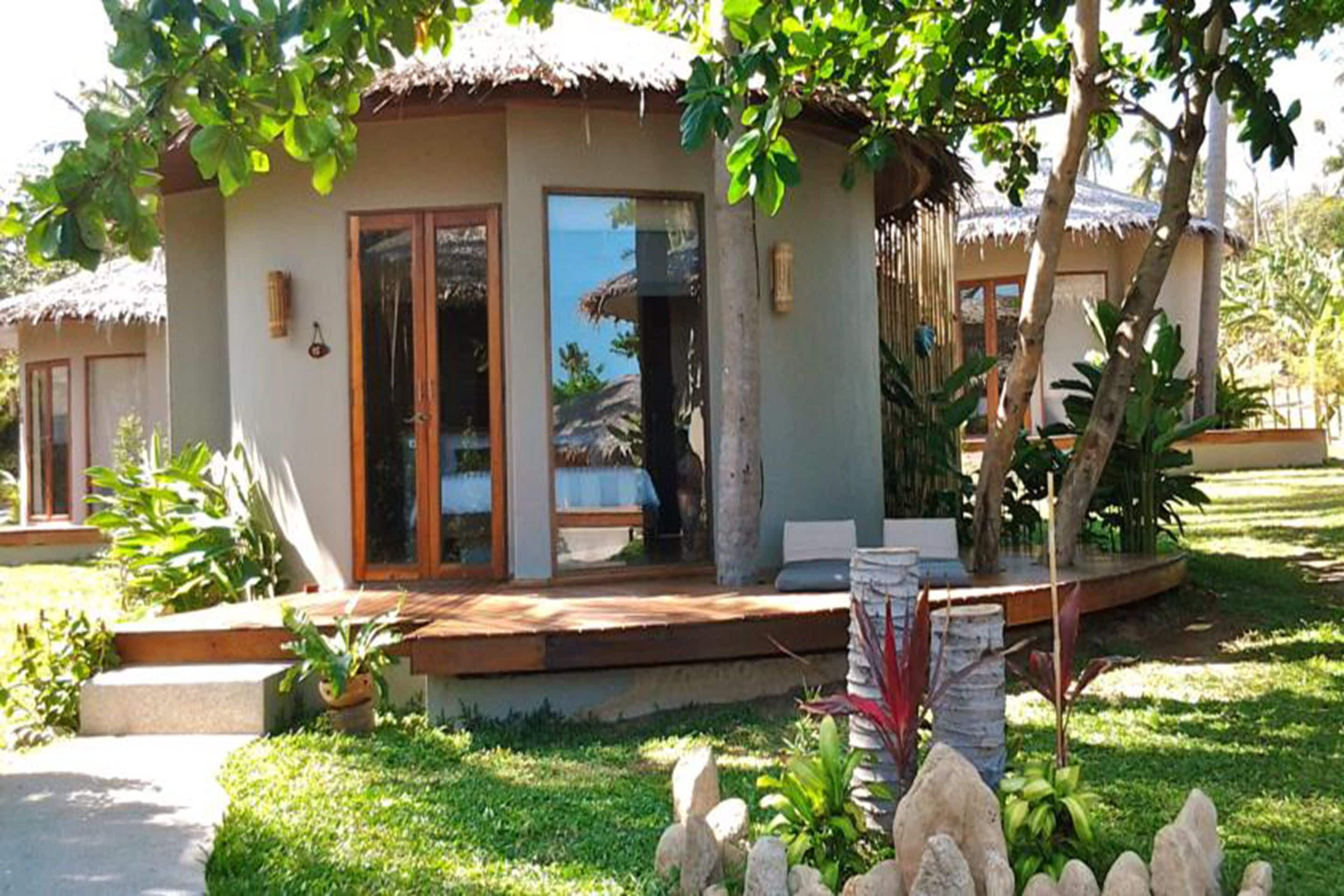 Ein Bungalow mit einem Reetdach, einer Glastür und einer kleinen Veranda mit Sitzgelegenheit.
