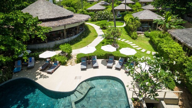 Un resort con piscina, sillas de descanso y cabañas de techo de paja.