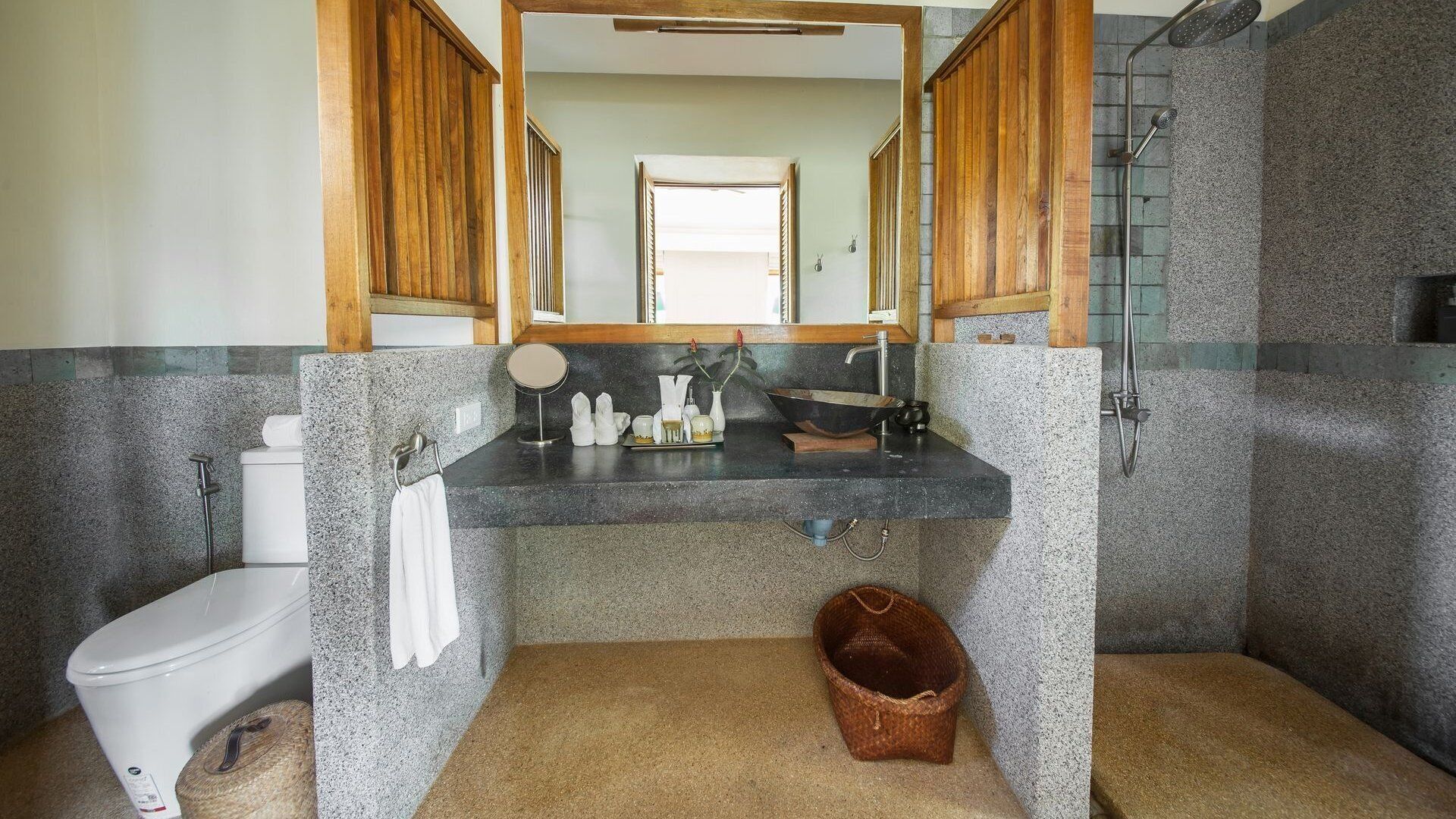 A bathroom with a granite countertop, a white toilet, a sink with a mirror, and a shower area.