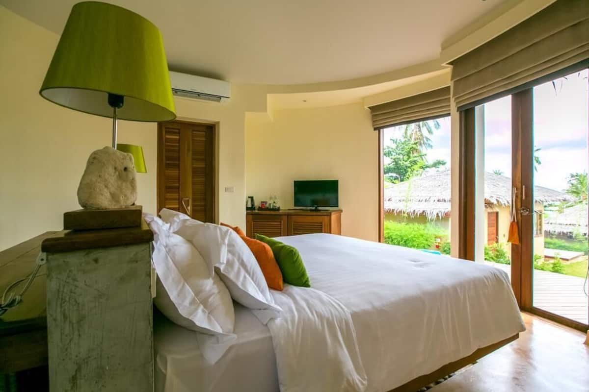 Ein Schlafzimmer mit Bett, Lampe, Fernseher und Blick ins Freie.