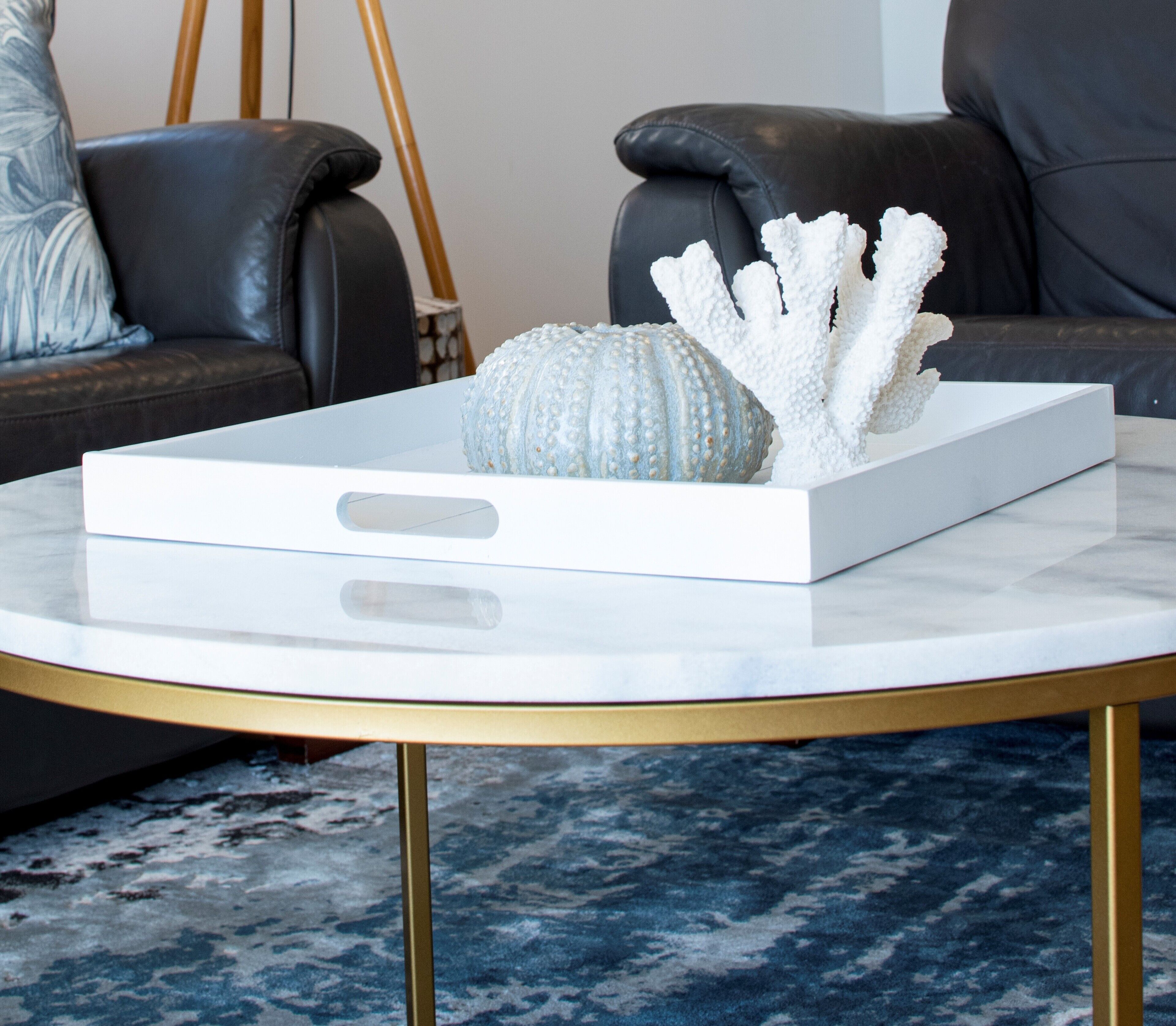 A white box with a handle on a round table with gold legs, containing a decorative object and a shell.