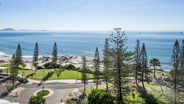 A coastal view with a road leading to a beach, surrounded by trees and a clear sky.
