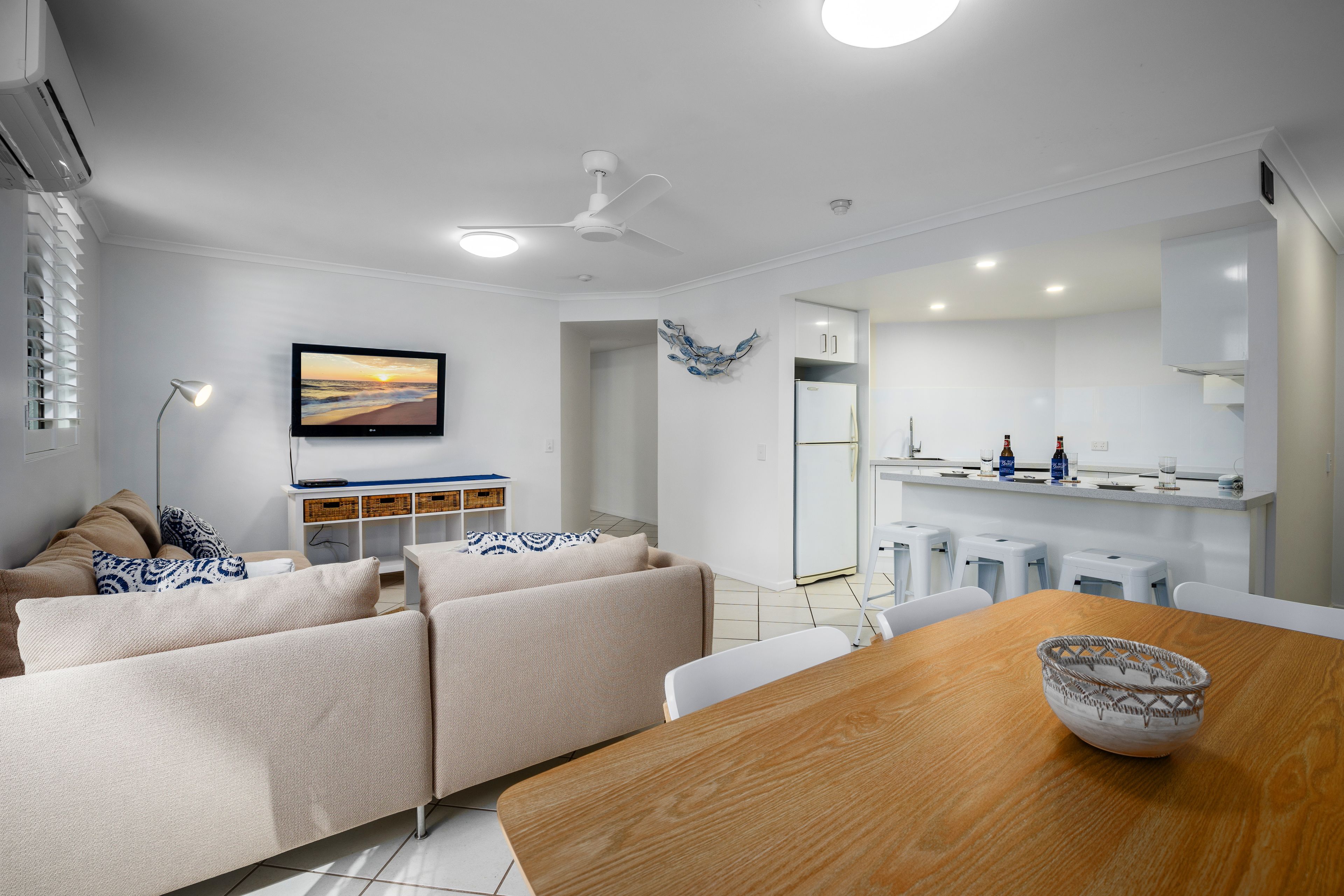 A modern kitchen with white cabinets, a dining table with a bowl, and a ceiling fan.
