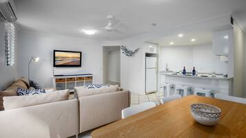 A modern kitchen with white cabinets, a dining table with a bowl, and a ceiling fan.