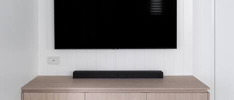 Een flatscreen televisie bevestigd aan een muur boven een houten entertainmentmeubel met kastjes.
