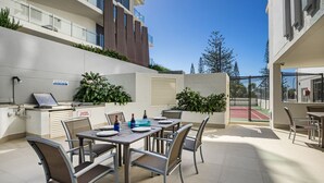 A patio with a table set for dining, outdoor seating, and a tennis court in the background.
