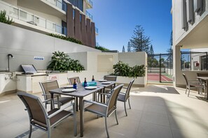 A patio with a table set for dining, outdoor seating, and a tennis court in the background.