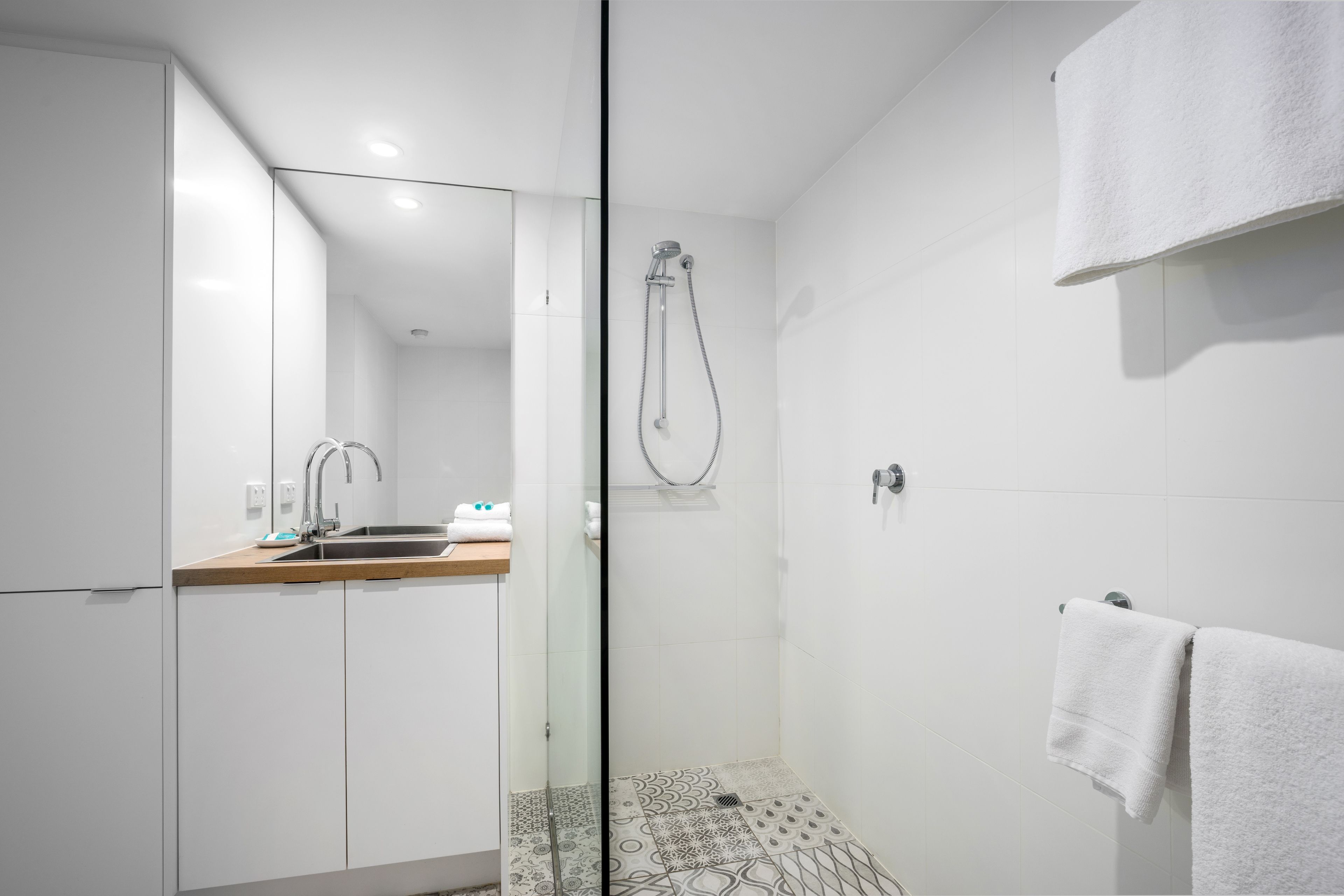 A modern bathroom with a glass shower enclosure, a sink with a wooden countertop, and a towel rack.
