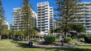 A modern multi-story building with balconies, surrounded by greenery and a clear blue sky. - Pacific Beach Resort (Mooloolaba)