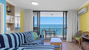 A living room with a striped sofa, a small table, and a view of the sea through a glass door.