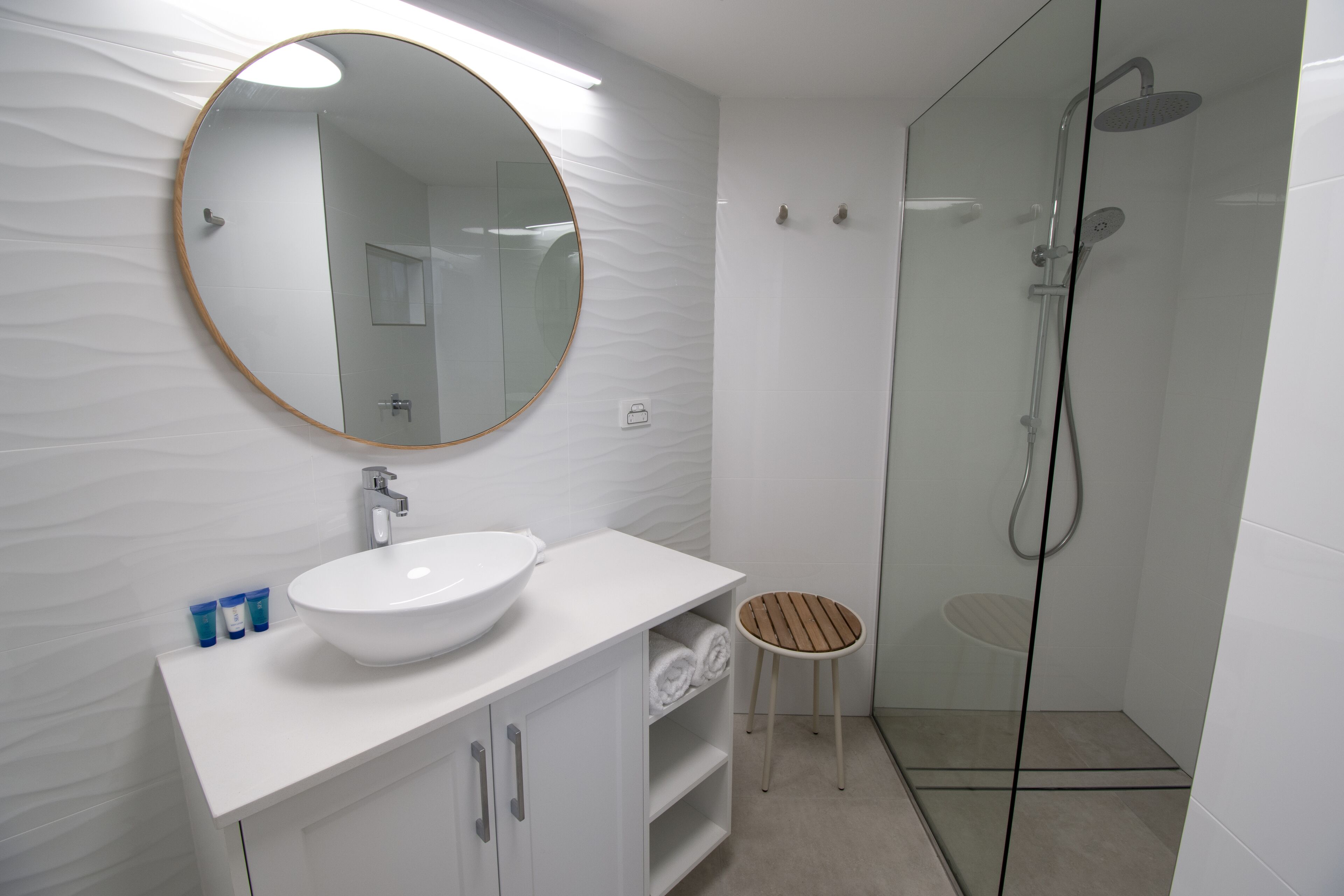 A modern bathroom with a round mirror, white sink, and glass-enclosed shower.