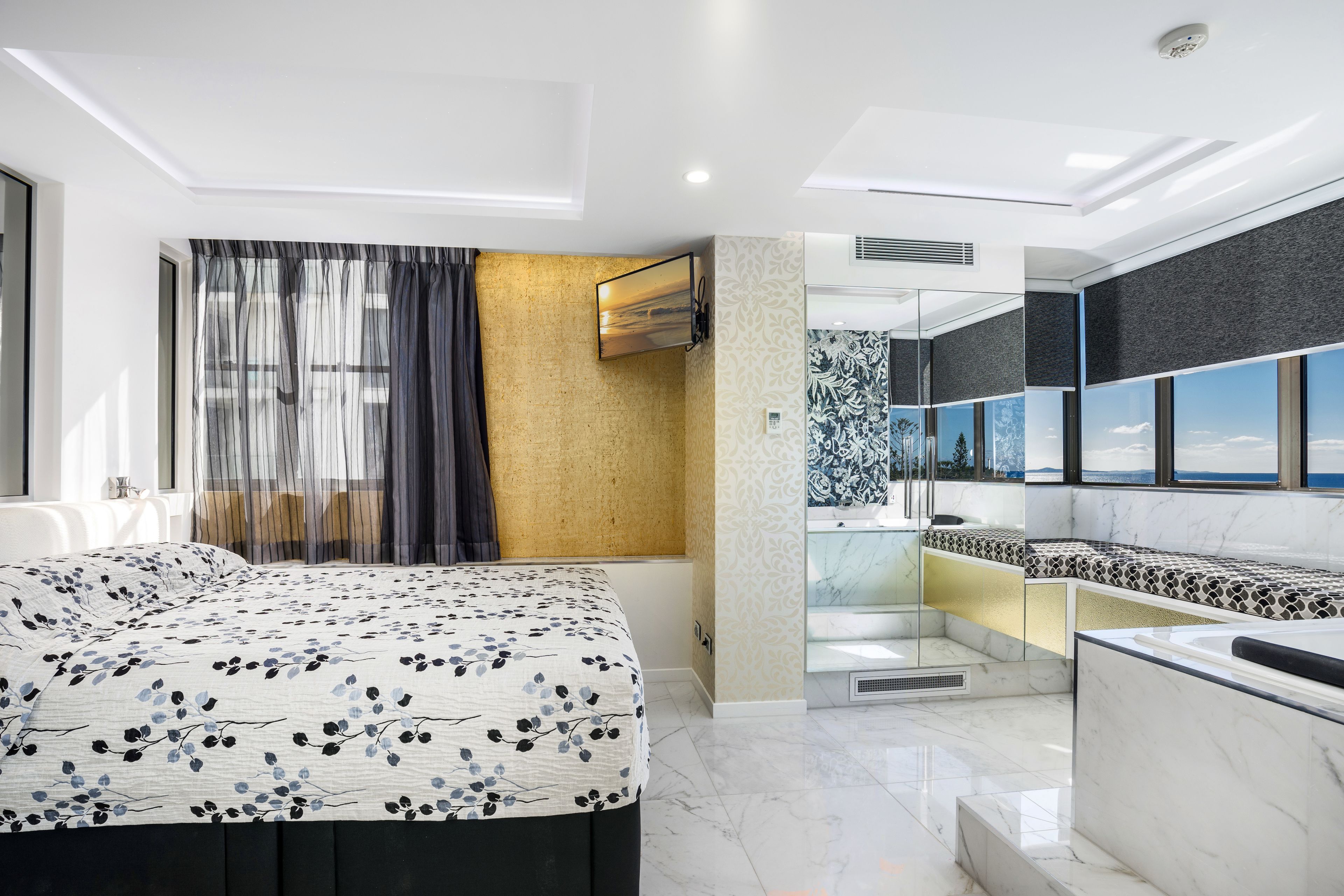 A modern hotel room with a large bed, a bathroom with a bathtub, and a view of the mountains.