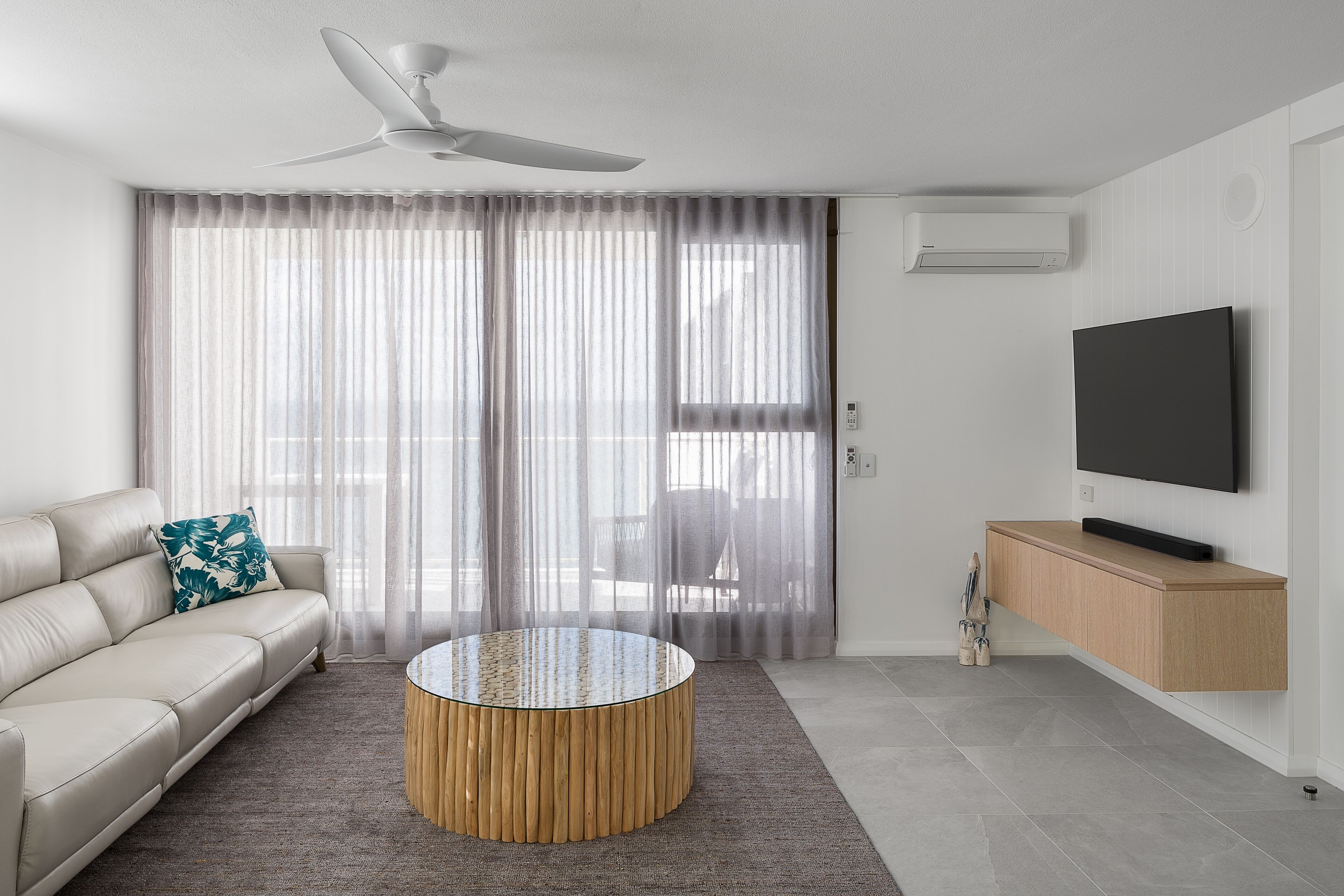 A modern living room with a sofa, a round coffee table, a TV on a wooden cabinet, and a ceiling fan.