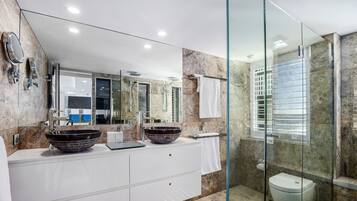 A modern bathroom with a glass-enclosed shower, a double sink with a large vessel sink, and a marble-tiled vanity.
