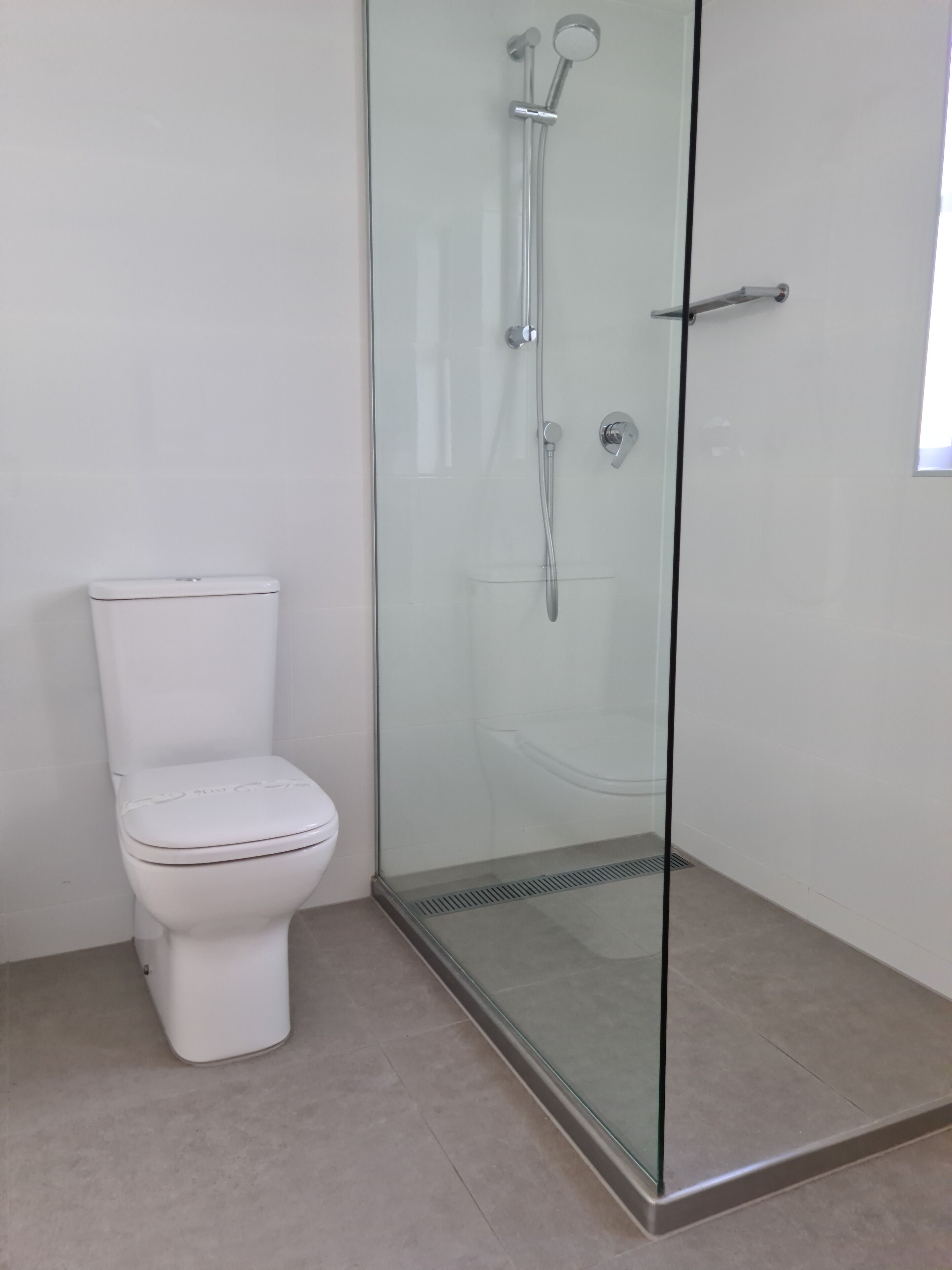 A bathroom with a glass-enclosed shower, a white toilet, and a tiled floor.
