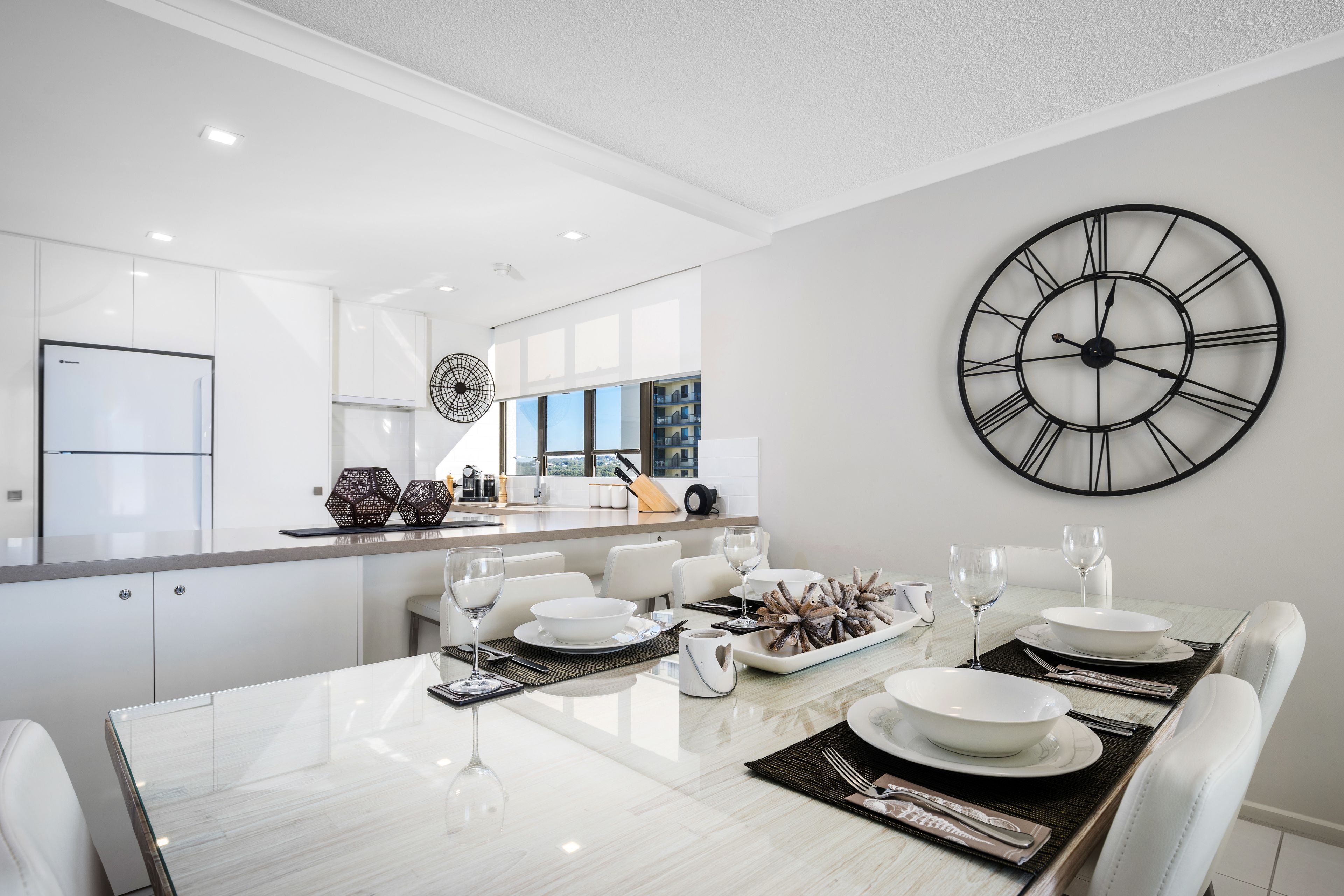 A modern kitchen with white cabinetry, a large island, and a dining area with a marble table set for four.