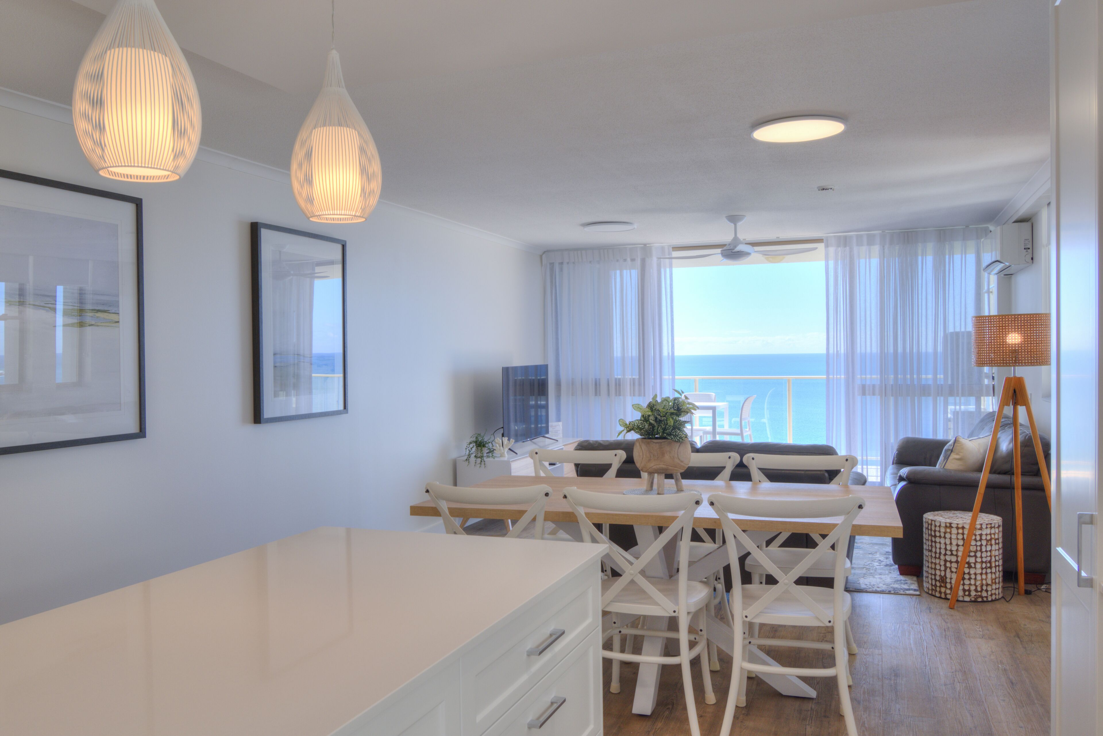 A modern living room with a dining area, large windows, and a view of the sea.