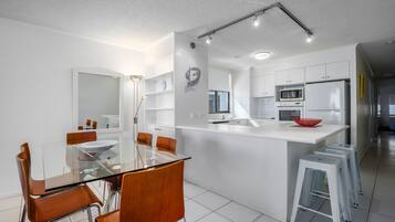 A modern kitchen with white cabinets, a central island, and a dining area with a glass table and wooden chairs.