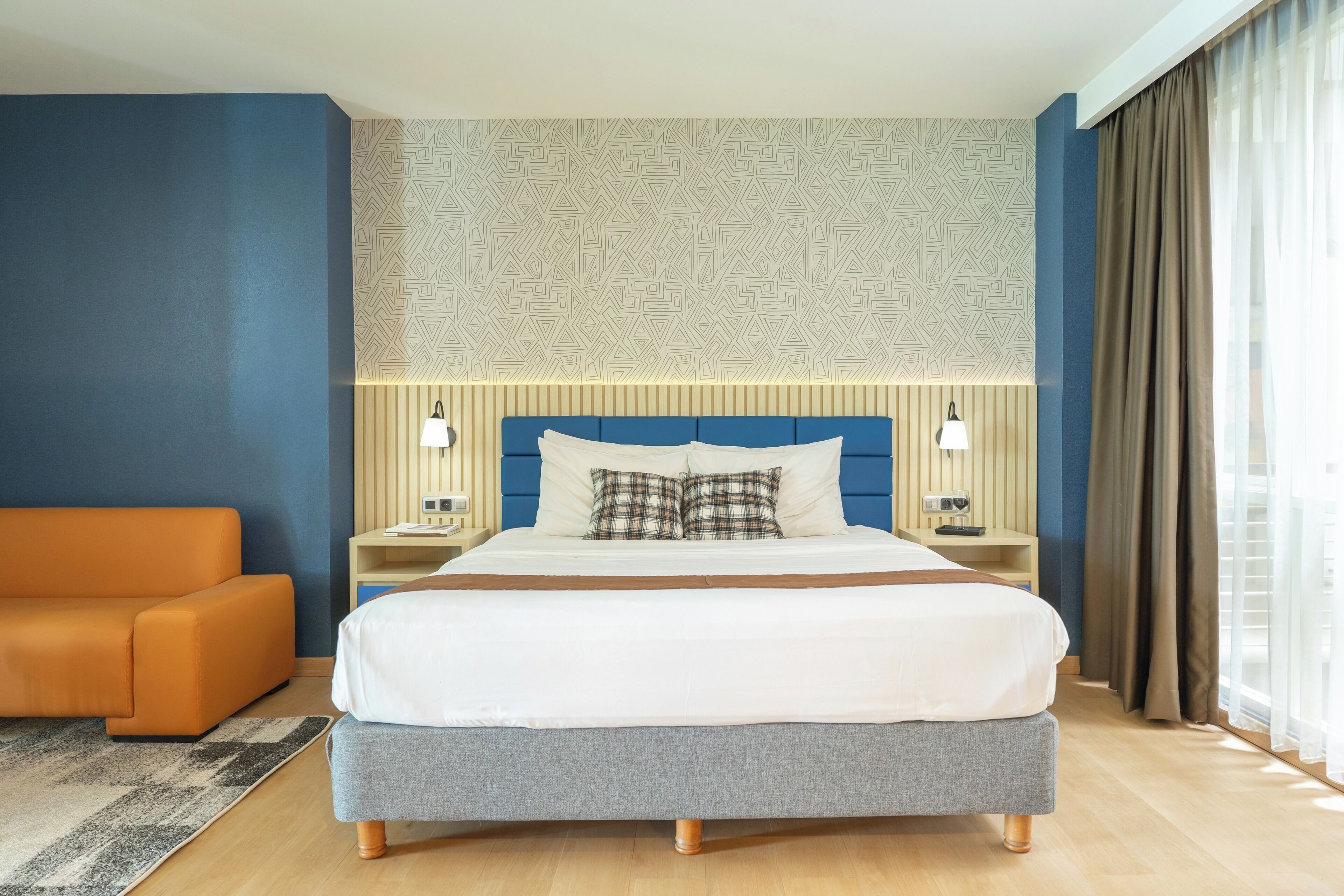 A modern hotel room with a large bed, a nightstand, a lamp, and a sofa.