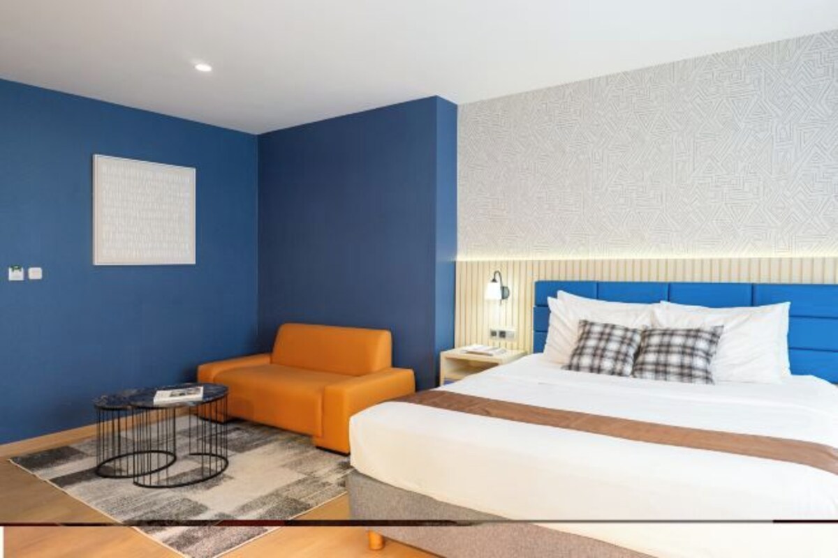 A hotel room with a large bed, a sofa, a small table, and a nightstand.