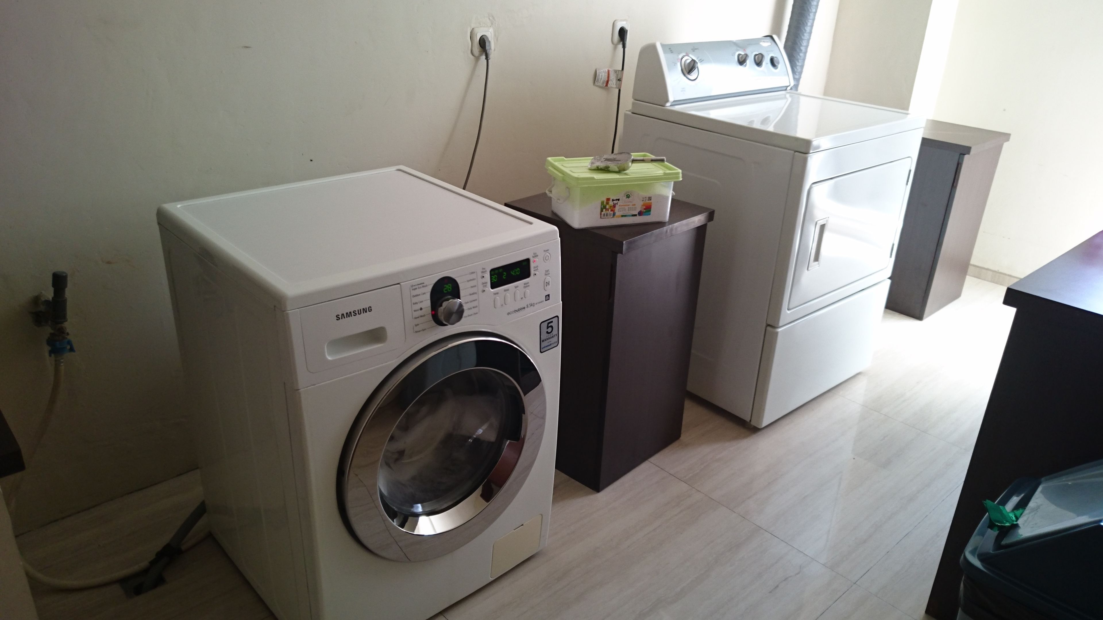 A compact laundry area with a front-loading washing machine, a dryer, and a small cabinet with a green lid.