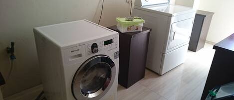 A compact laundry area with a front-loading washing machine, a dryer, and a small cabinet with a green lid.