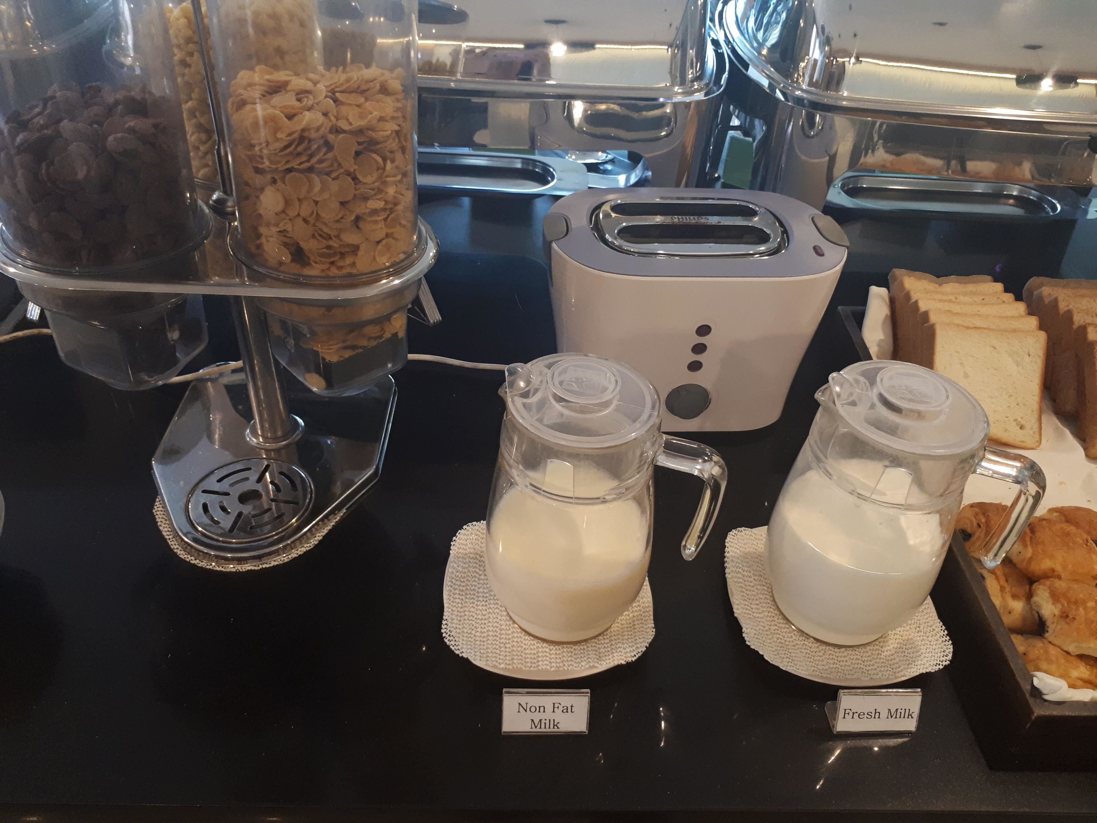 Un buffet de petit-déjeuner proposant du lait écrémé et du lait entier, différents types de céréales et un grille-pain.