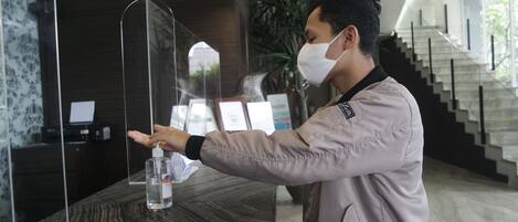 A person using a hand sanitizer dispenser at a reception desk with a modern design, a staircase, and framed certificates in the background.