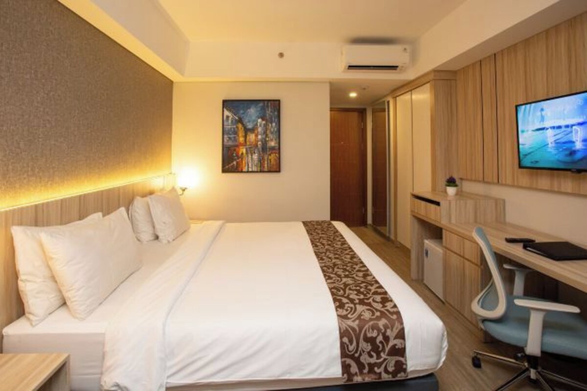 A hotel room with a bed, a desk, a chair, a television, and a painting on the wall.