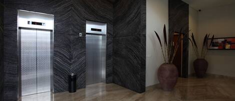 Un área de ascensores moderna con dos ascensores, suelo de mármol y jarrones decorativos.