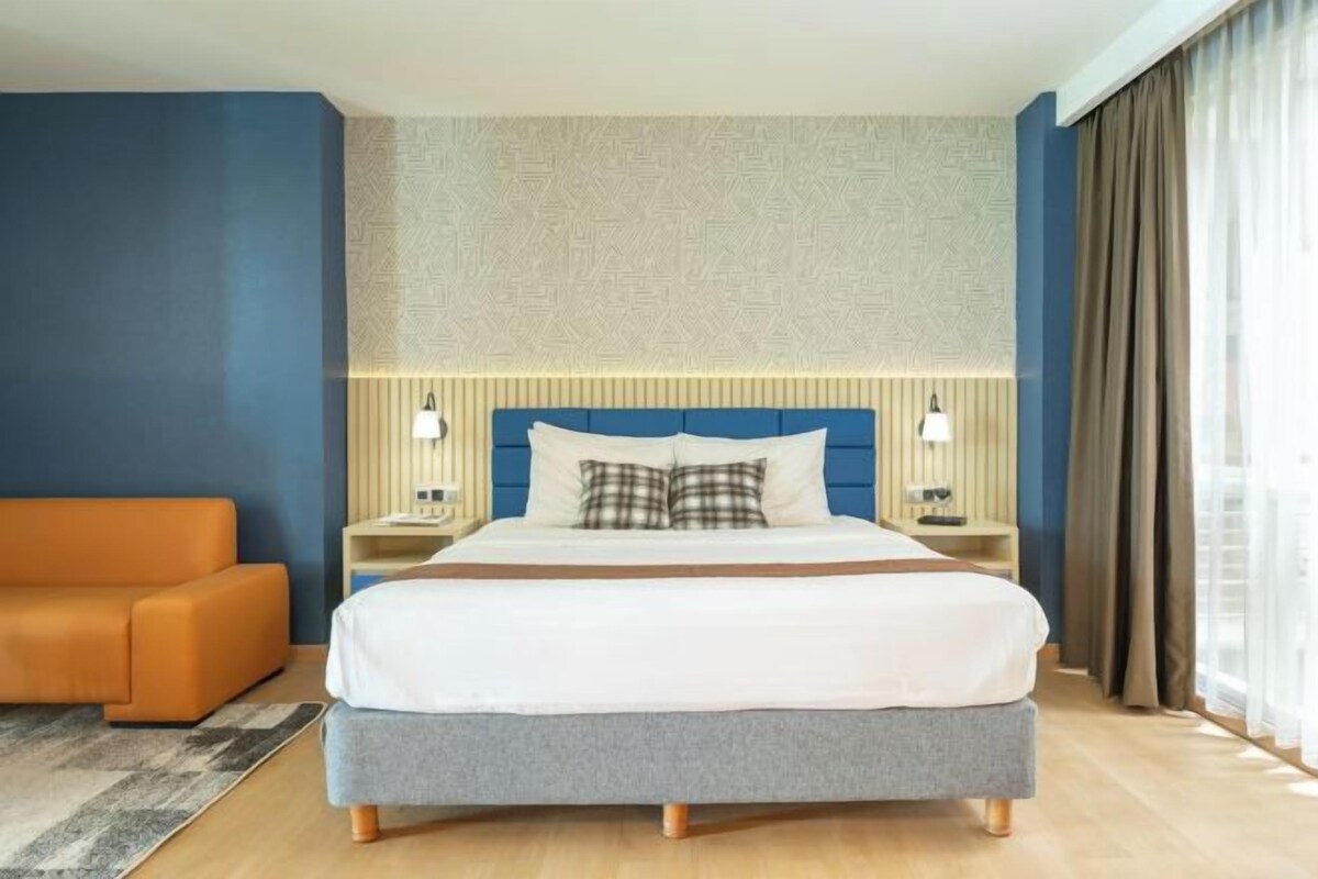 Ett modernt hotellrum med en stor säng, två sängbord, ett litet bord, en soffa och utsikt över omgivningarna.