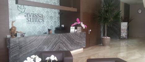 A reception area with a marble counter, two sofas, a potted plant, and a large potted tree.