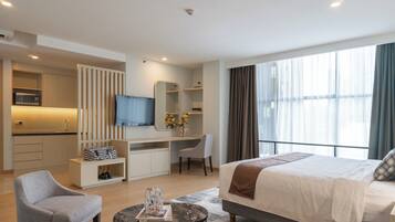 Habitación de hotel moderna con cama, escritorio, silla, televisor y kitchenette.