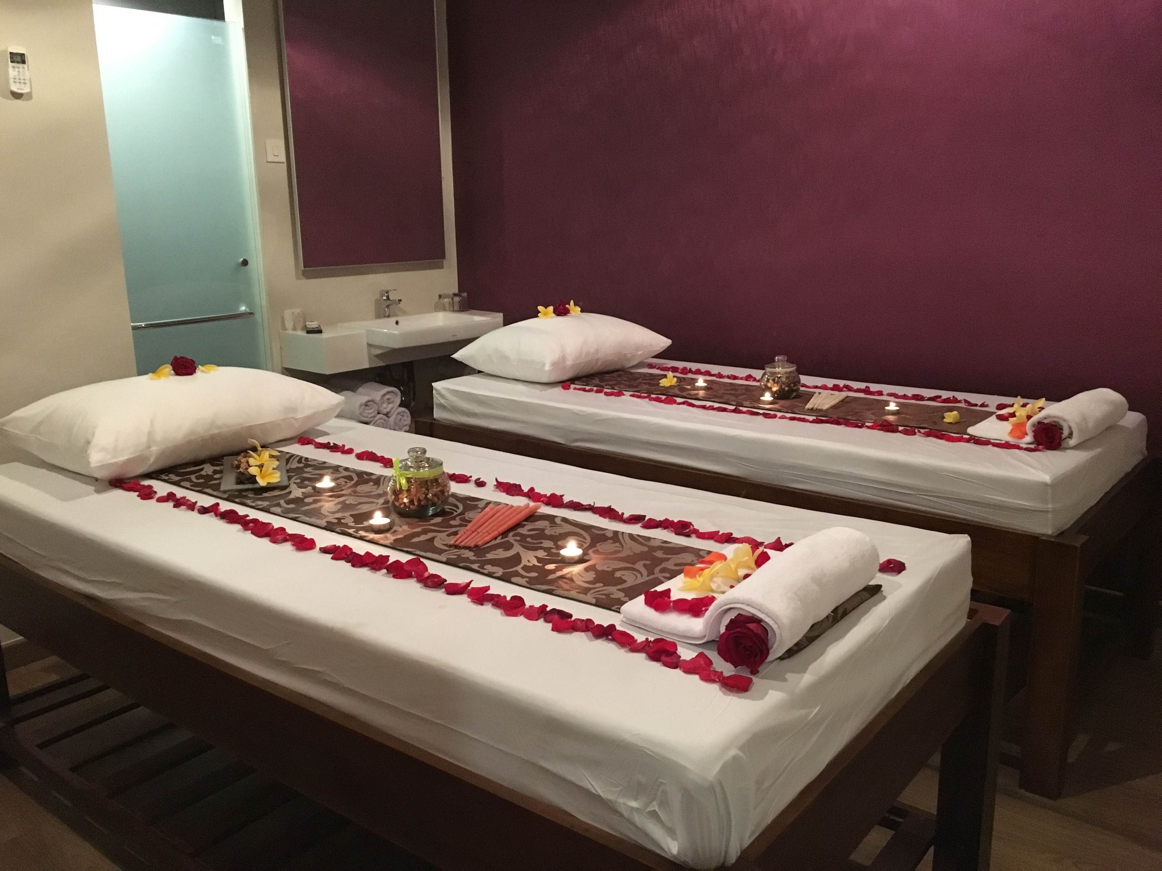 Two massage beds with white linens, rose petals, candles, and towels.