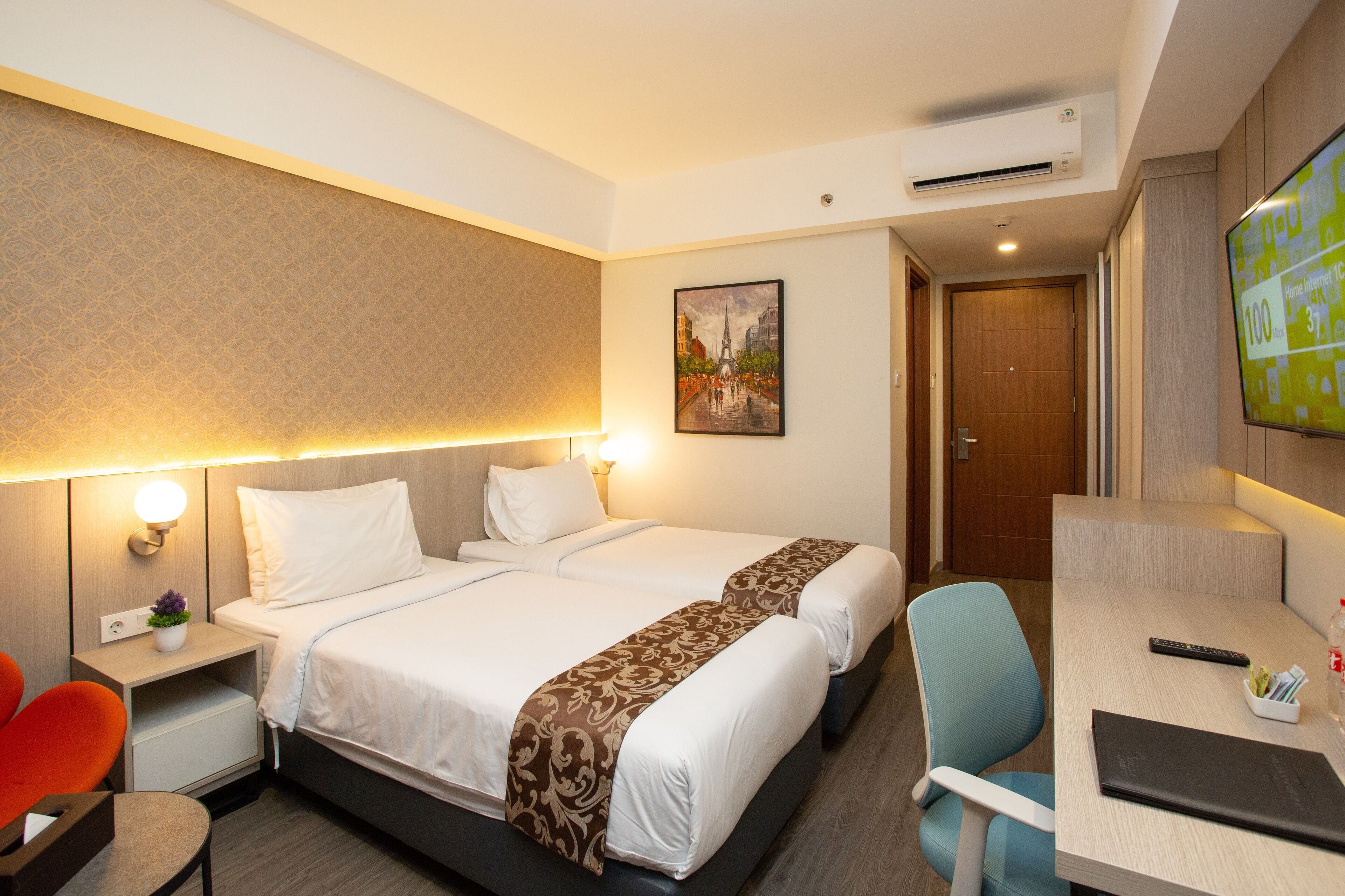 A hotel room with a bed, bedside tables, a desk, a chair, a TV, and a painting on the wall.