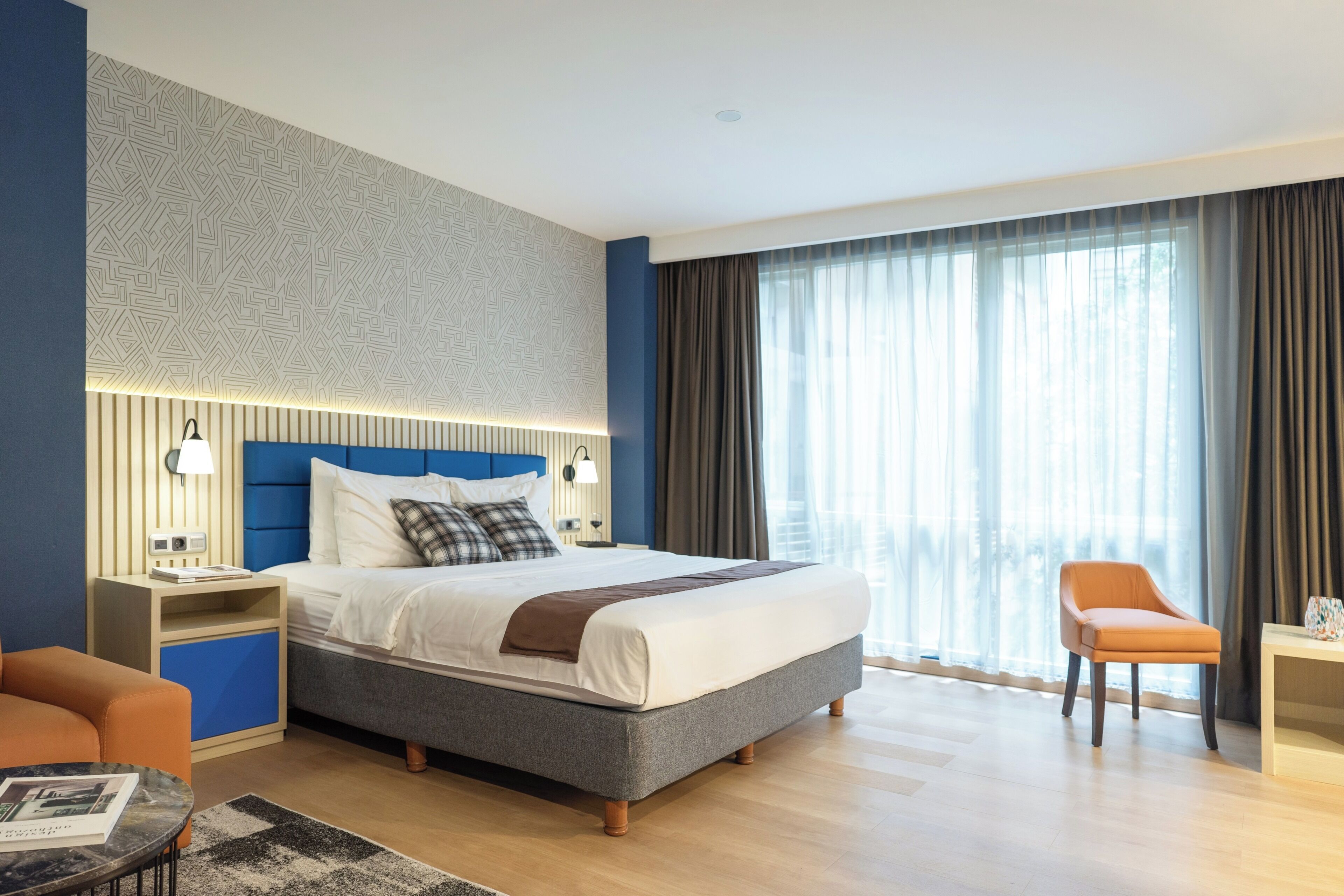 Une chambre d’hôtel moderne avec un grand lit, une table de chevet, une chaise et une fenêtre avec des rideaux.