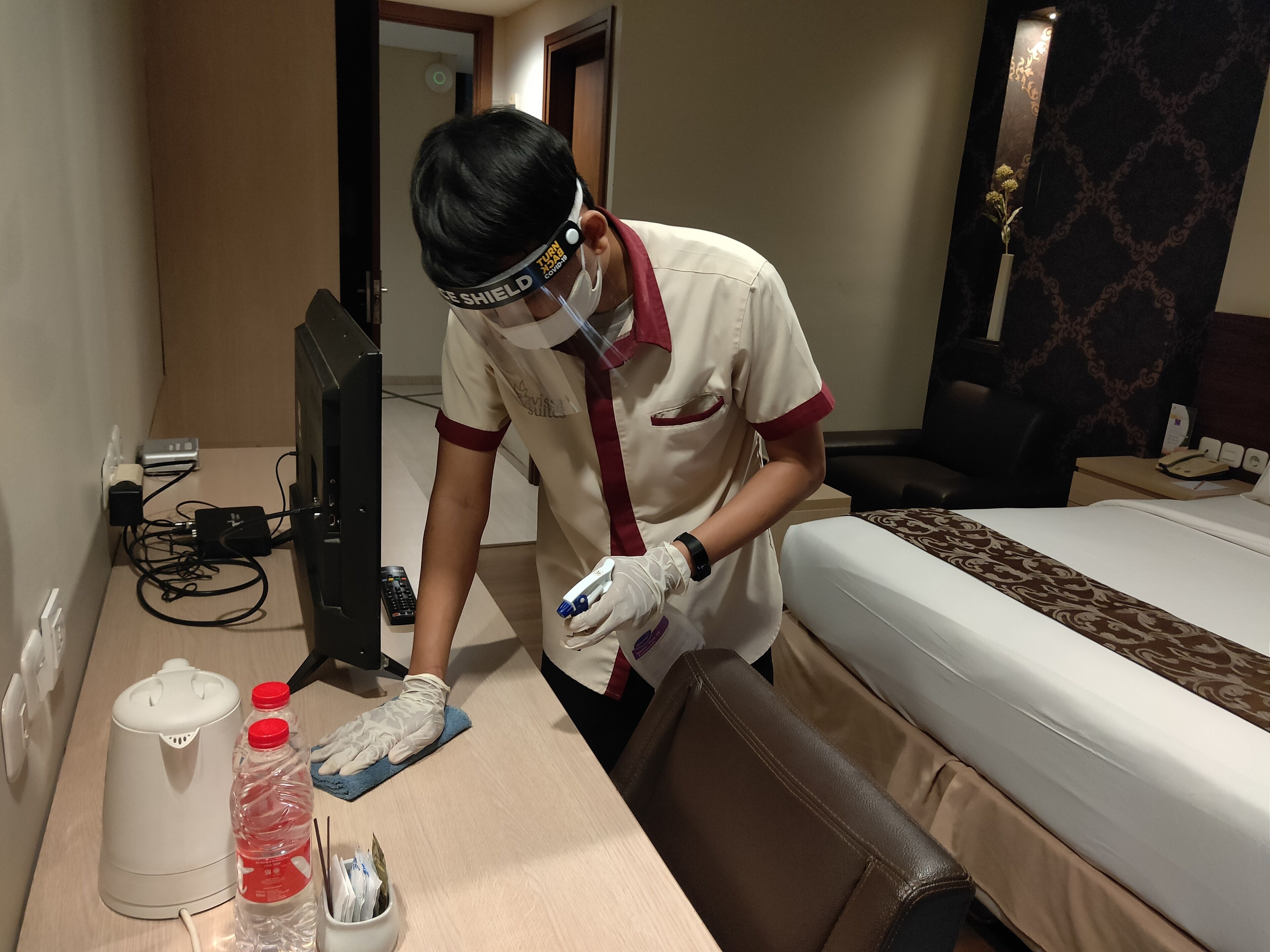 Une chambre d’hôtel avec un lit, un bureau équipé d’un ordinateur, une bouteille d’eau et une télécommande.