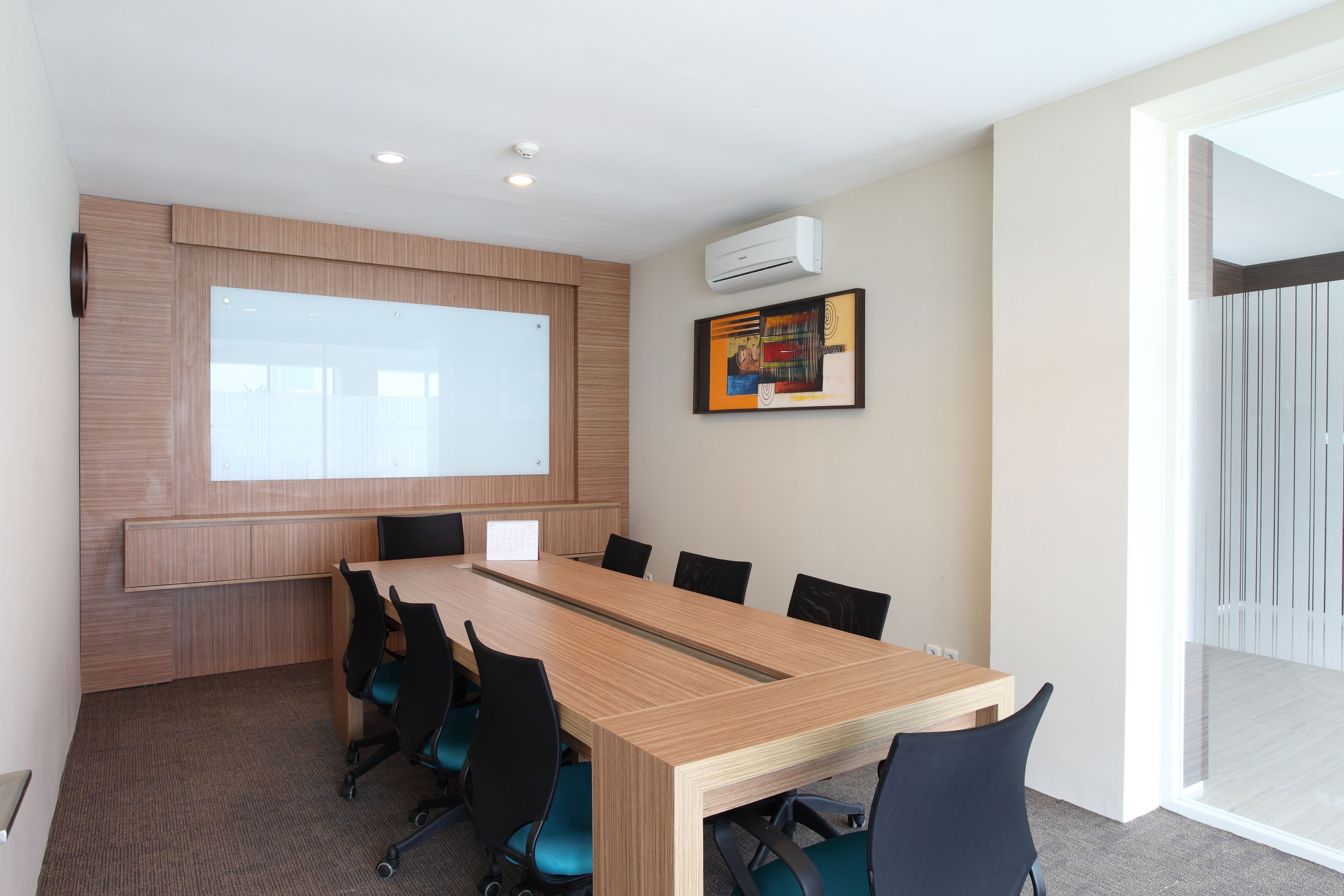 A conference room with a long table, six chairs, a projector screen, and an air conditioning unit on the wall.