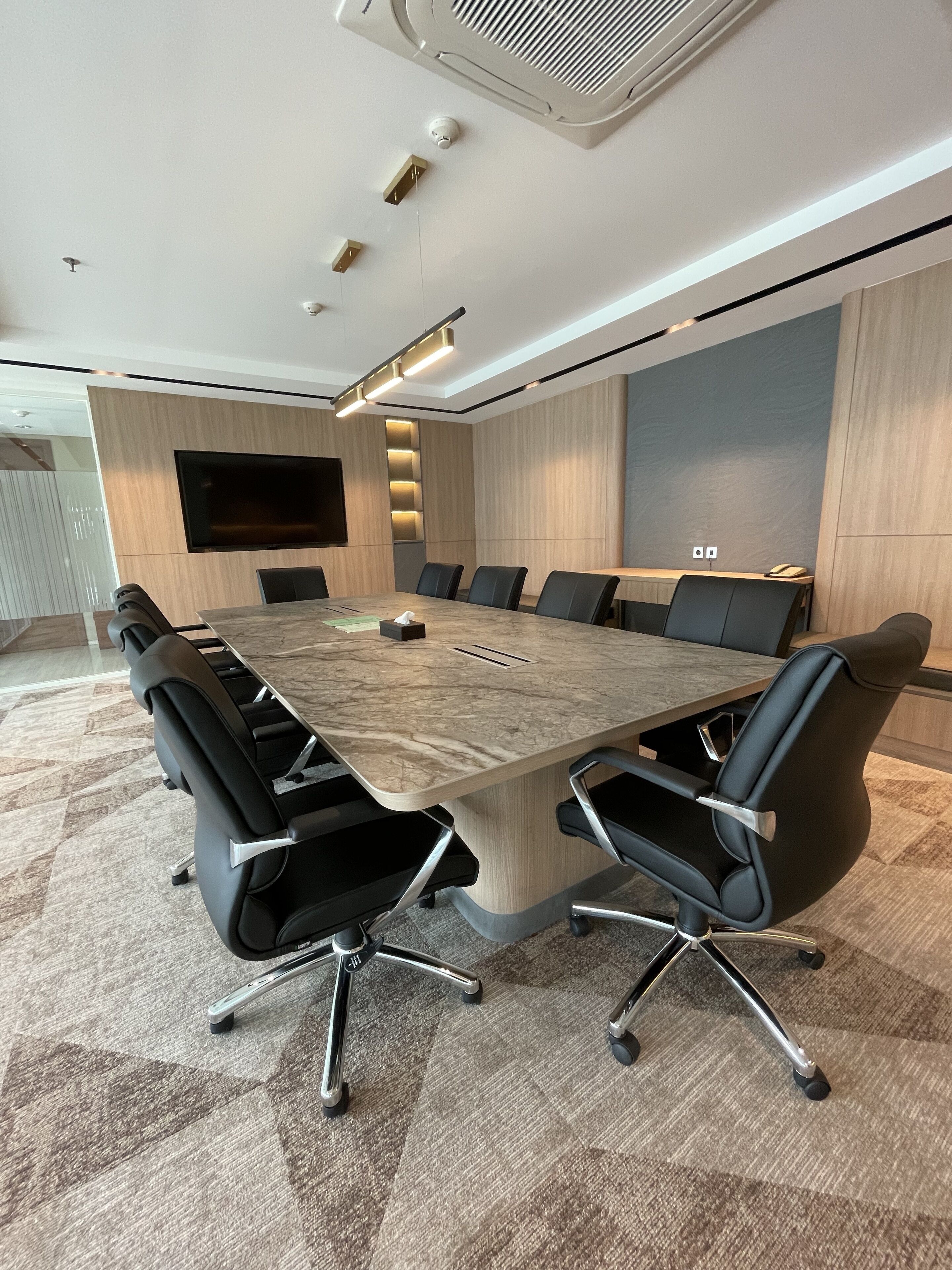 A conference room with a large table, black chairs, a mounted TV, and recessed lighting.