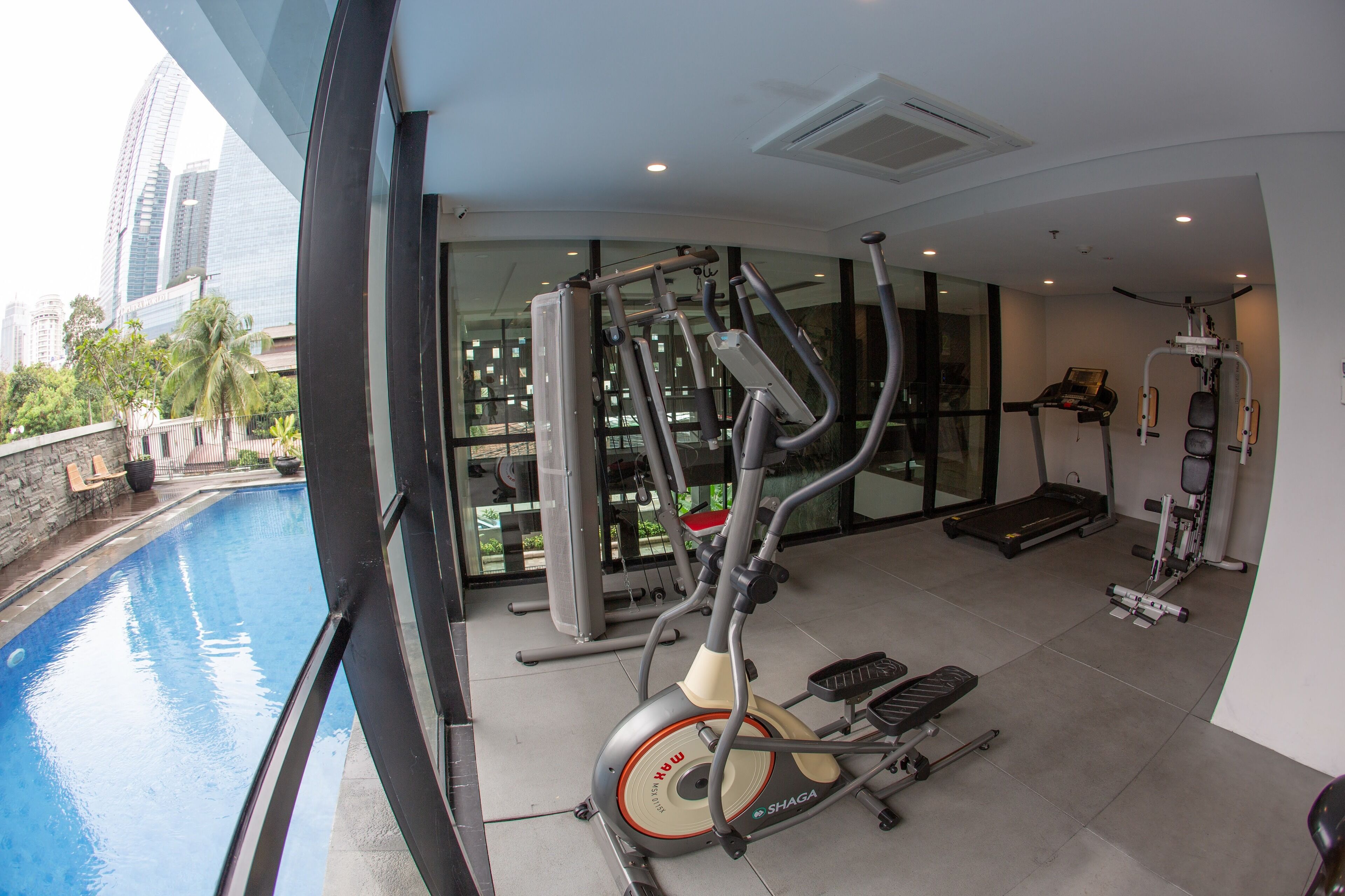 A gym with various exercise equipment, a pool, and a city view.
