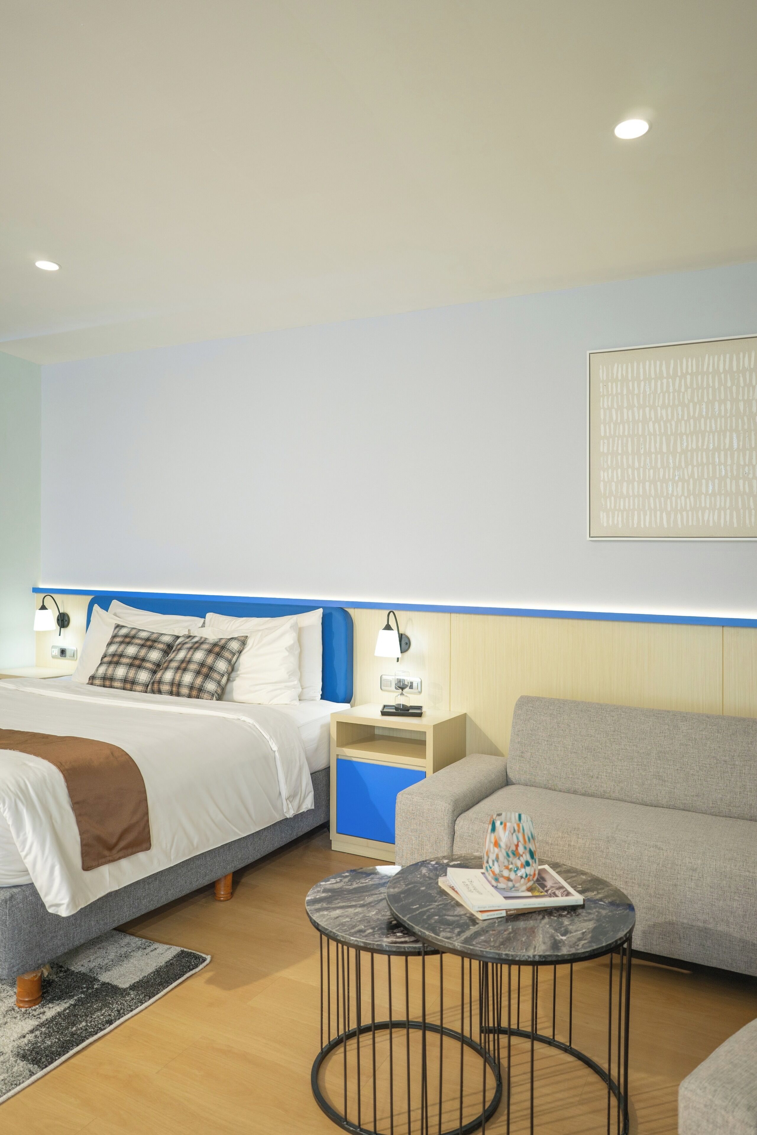Une chambre d’hôtel moderne, équipée d’un lit, d’un canapé, d’une petite table ronde et d’une œuvre d’art accrochée au mur.