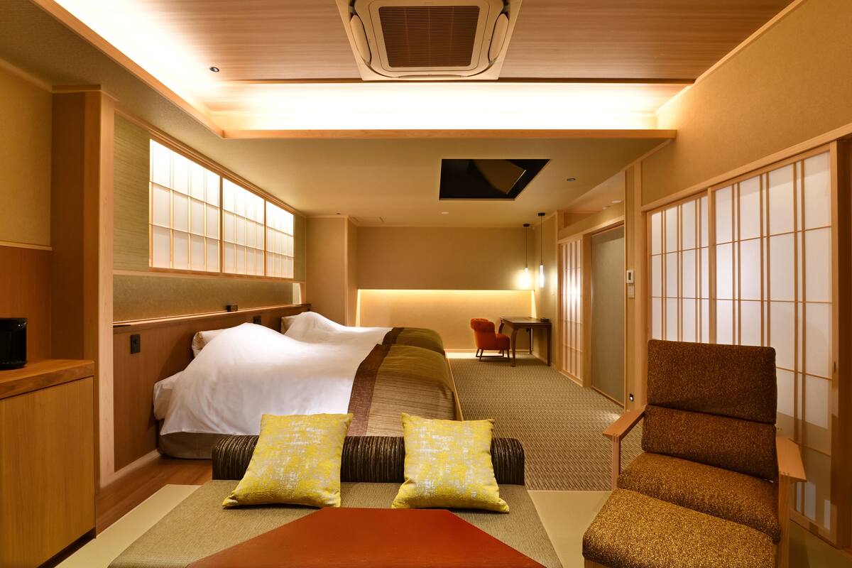 Ein Hotelzimmer mit Bett, einer Sitzecke mit Kissen, einem Tisch und traditionellen Schiebetüren.