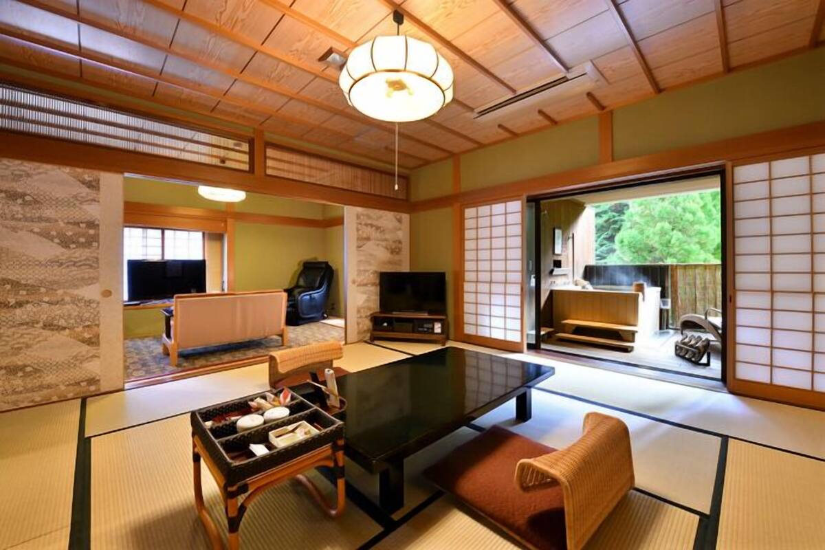 Ein traditioneller japanischer Raum mit Tatami-Boden, einem niedrigen Tisch, einer Couch und Schiebetüren zu einem Garten.
