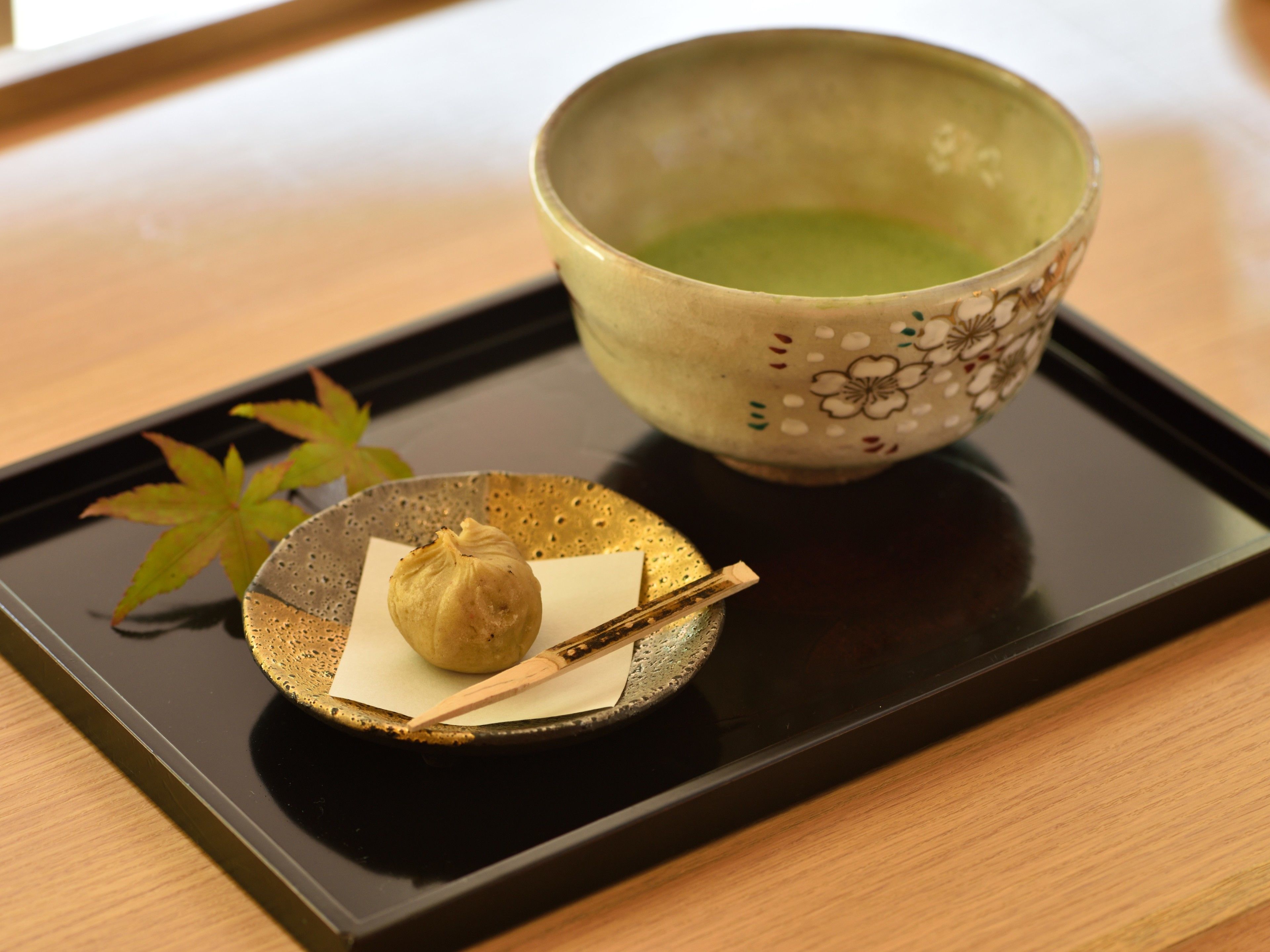 A tray with a bowl of green tea, a small dish with a dumpling, and a pair of chopsticks on a wooden table.