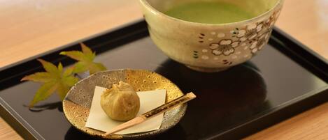 A tray with a bowl of green tea, a small dish with a dumpling, and a pair of chopsticks on a wooden table.