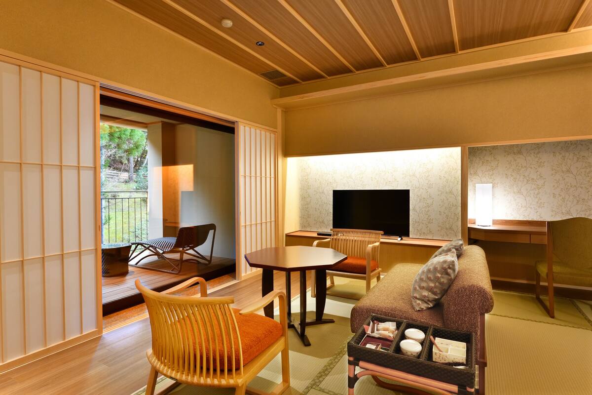 Ein traditioneller japanischer Raum mit Tatami-Boden, einem niedrigen Tisch, einer Couch und einem Fernseher.