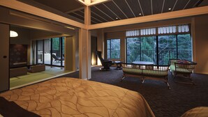 Ein geräumiges Hotelzimmer mit einem großen Bett, einem Esstisch, Schaukelstühlen und Blick ins Freie durch große Fenster.